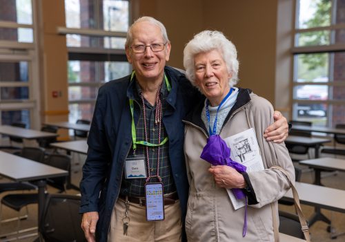 An older man and woman embrace from the side and smile towards the camera.