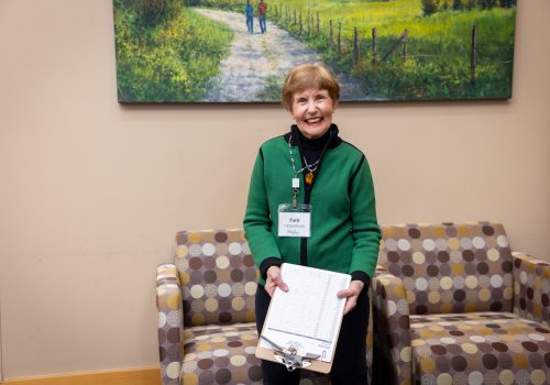 A smiling older woman holds a clipboard.