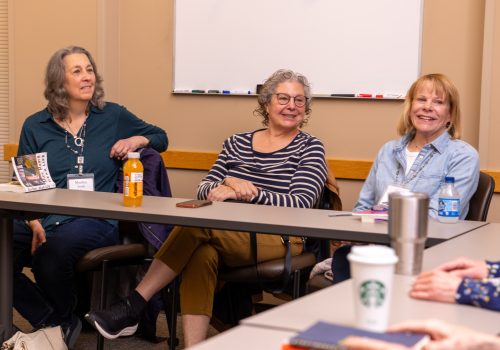 Three smiling women sitting at a classroom table