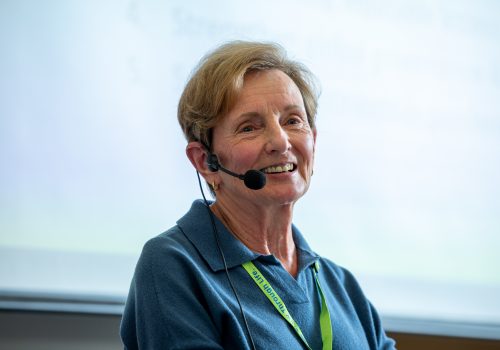 An older woman wearing a headset microphone smiles.