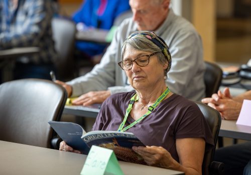 Older woman sits in a classroom, looking at a book.